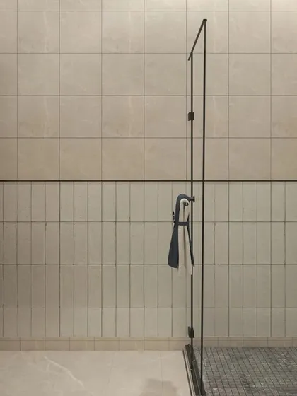 This view shows the clean and simple design of the shower area. The combination of vertical and horizontal tiles adds subtle texture, while the glass partition keeps the space feeling open and bright.