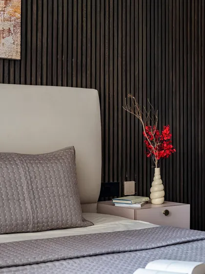 A close-up of the bedside, where a vibrant red floral arrangement provides a pop of color against the dark, reeded wall and neutral bedding.