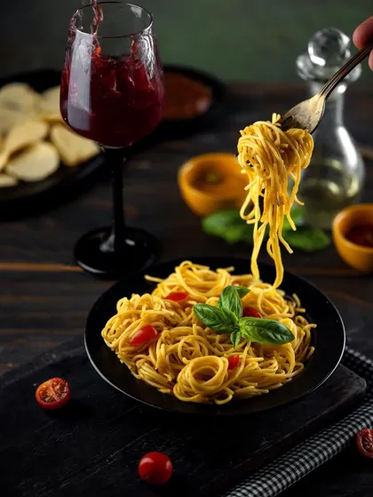 A plate of Hakka noodles paired with a glass of red wine. The dark, moody lighting creates a sophisticated, dinner-time atmosphere, elevating a simple dish into a gourmet experience.