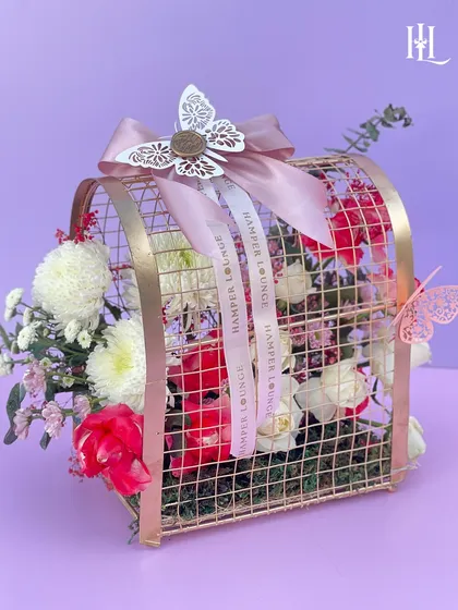 A detailed shot of the metal birdcage floral hamper, showing the mix of red and white flowers inside. The butterfly accents add a touch of whimsy.