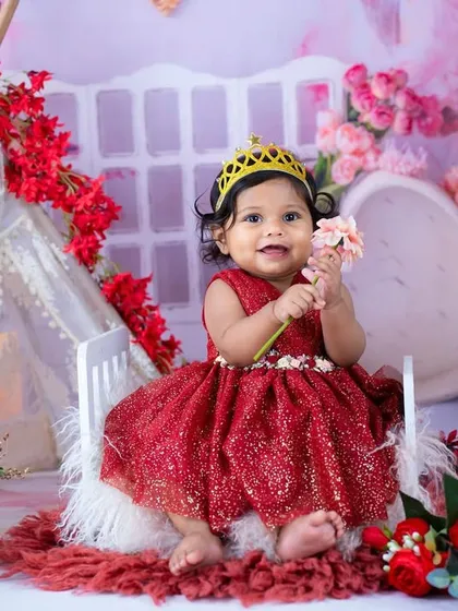A little princess in a sparkly red dress, holding a flower. The red and pink floral background creates a vibrant and festive feel.