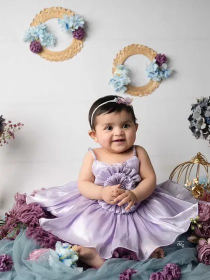 A vision in lavender. This baby girl is surrounded by a beautiful arrangement of purple and blue florals, decorative birdcages, and soft fabrics for her milestone session.