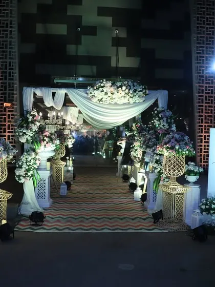 A nighttime view of this elegant white-draped entrance, where soft lighting and hanging greenery create a dreamy and romantic pathway for an evening celebration.