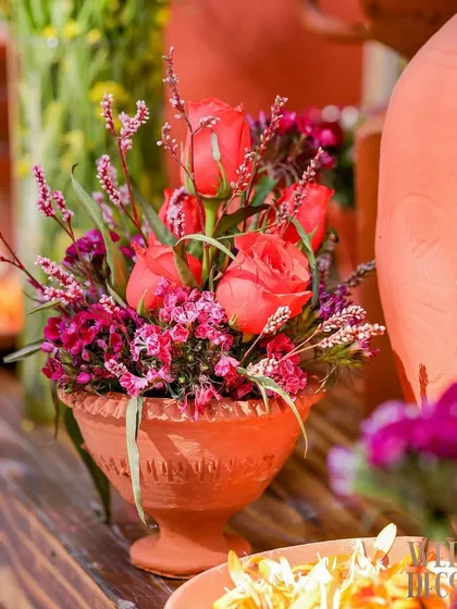 A small terracotta pot holding a delicate arrangement of pink roses and filler flowers. This shows the variety of florals used to add pops of different colors throughout the venue.