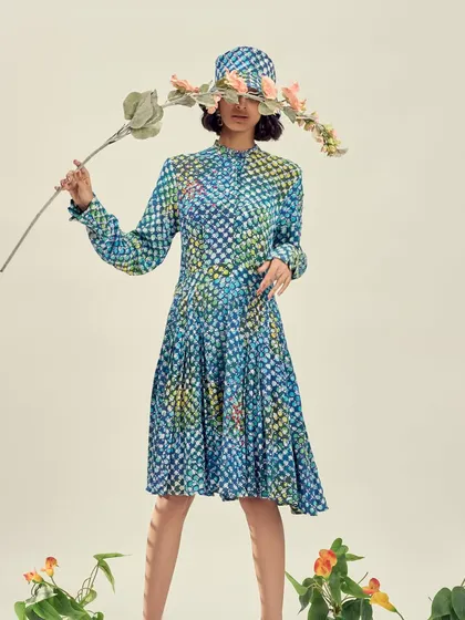 An artistic editorial image where the model's face is obscured by a flower, drawing all attention to the printed dress and matching hat. This conceptual styling choice creates a surreal and memorable fashion photograph.