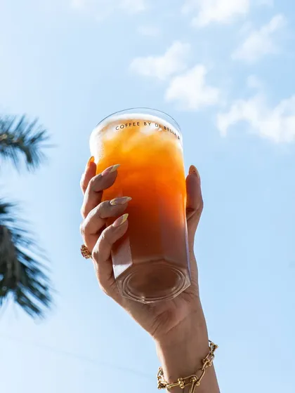 An iced coffee held up against a bright blue sky. This is an aspirational, lifestyle-focused shot that evokes feelings of summer and freedom.