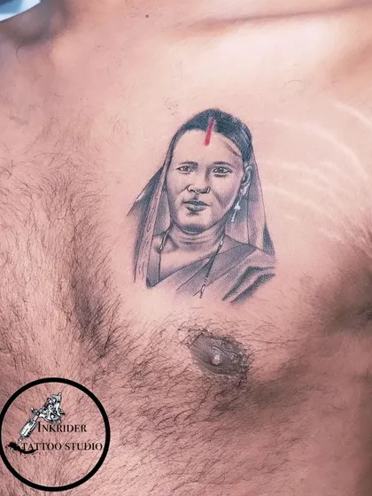 A chest portrait tattoo honoring a mother. The red bindi adds a touch of color and cultural significance to this beautiful black and grey piece.