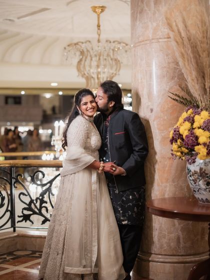 A sweet, candid moment between the couple during their Sangeet. Her ivory outfit and his classic black ensemble create a timeless and elegant look against the grand backdrop.
