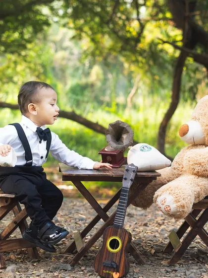 This little gentleman is the perfect host for his teddy bear picnic. The lush green background of the park creates a beautiful, natural setting.