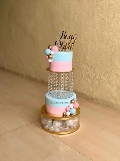 A beautiful two-tier gender reveal cake in pink and blue. This design features a crystal separator filled with pearls and a "Boy or Girl" topper.