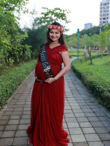 A solo portrait of a client in our wine-colored A-line gown, accessorized with a "Mom to Be" sash and a floral crown. This shows how you can personalize your rental for a baby shower or photoshoot.