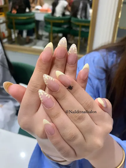 A delicate summer design with pale yellow French tips and hand-painted white daisy accents on almond-shaped nails. A fresh and cheerful look for any day.