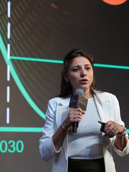 A speaker presents on a technical topic, with a graph in the background illustrating future trends and projections.