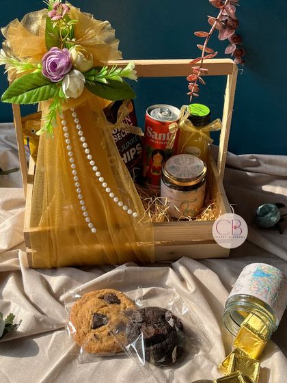 Unwrap the joy of love with our confectionery delight, perfect for an engagement or wedding favour. This pinewood basket is filled with cookies, snacks, a drink, and a handmade candle.