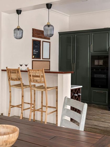 This kitchen, featured in a magazine, includes a small bar area with bamboo stools. The dark green cabinetry and wooden countertop create a cozy, rustic feel.