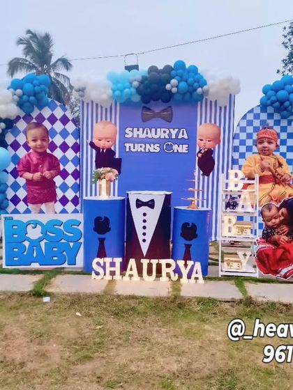 A wide shot of an outdoor Boss Baby party, showing the full scale of the setup on a grassy lawn. The decor includes personalized photo panels and multiple character props.