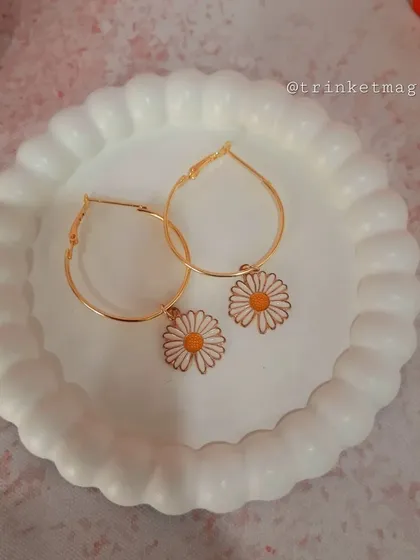 A pair of fresh and pretty daisy charm hoop earrings. The white and yellow enamel flower adds a cheerful touch to the simple gold hoops.
