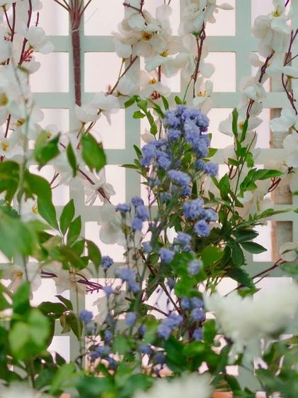 Detail of the floral work on the white trellis backdrop. Delicate white and purple blossoms are woven through the structure, adding a touch of natural beauty to the chic lounge area.