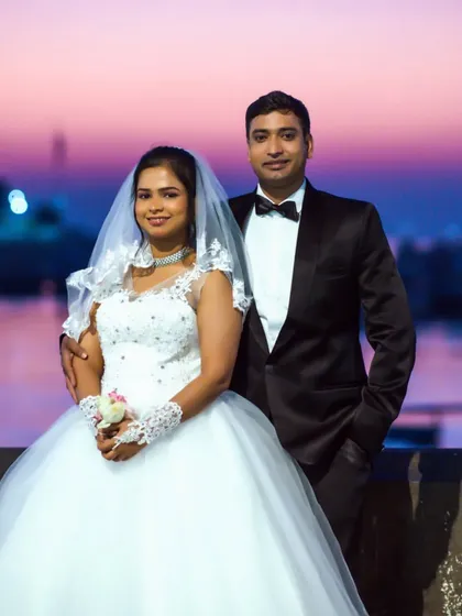 A classic portrait of a couple in their wedding attire against a beautiful sunset sky, perfect for a post-wedding or pre-wedding shoot.