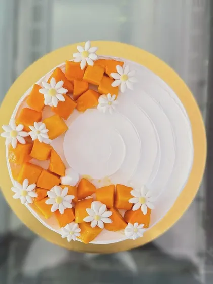 A fresh mango cake, topped with sweet mango chunks and delicate daisy flowers.
