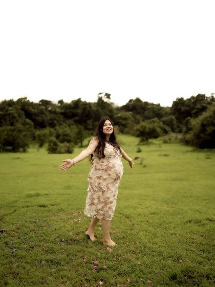 A portrait of pure freedom and joy. The mom-to-be stands in a green field with her arms outstretched, a picture of happiness and liberation.