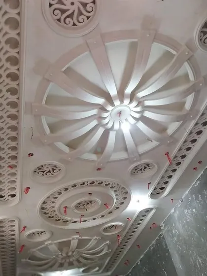 A highly detailed, multi-layered ceiling before painting. You can see the intricate circular patterns, jaali work, and radial designs that give it a palatial feel.