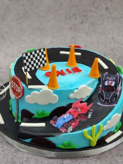 A racing track cake with two cars competing on a winding road, complete with a checkered flag and stop sign.