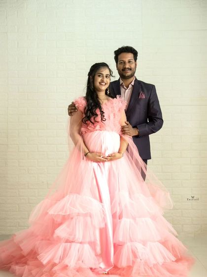A classic studio portrait of an expecting couple. The partner's dark suit provides a great contrast to the soft pink of the layered maternity gown.