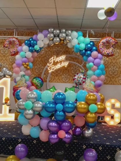 A colorful first birthday setup with a balloon ring, donut foil balloons, and light-up marquee numbers '1' and 'S'.