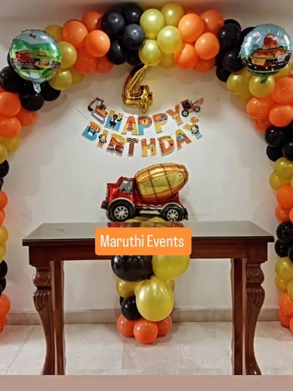 A construction-themed party for a 4th birthday. The orange, yellow, and black balloon arch is decorated with a cement mixer balloon and other construction vehicle cutouts.