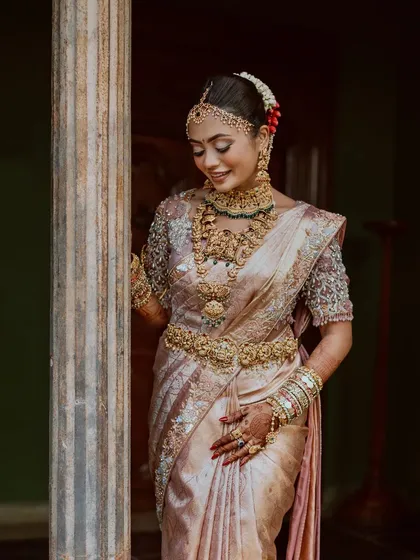 A bride in a pastel-hued saree, adorned with magnificent jewelry, leans against a pillar, the epitome of grace.