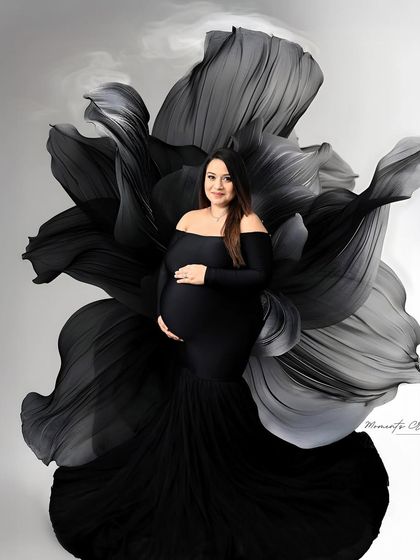 A bold and artistic statement. The mom-to-be is framed by a giant black floral prop, creating a dramatic, high-fashion silhouette that is both powerful and elegant.