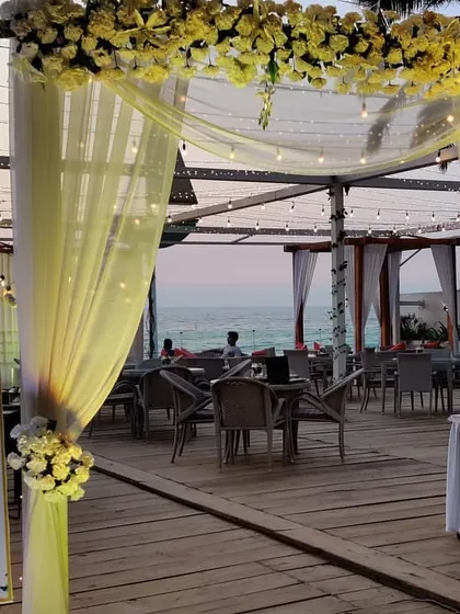 An evening engagement setup at a beach-facing restaurant. We used sheer yellow drapes, floral arrangements, and a personalized welcome sign to create an inviting entrance for the ceremony and dinner party.