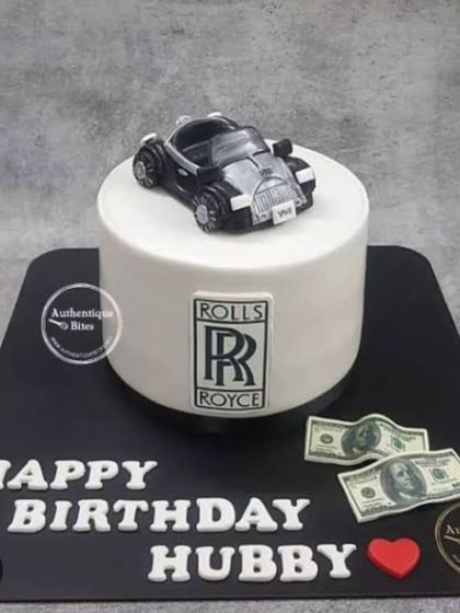 A classy Rolls Royce cake. This simple yet elegant design features the iconic logo, an edible car topper, and faux dollar bills.