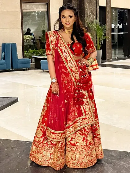 A perfect example of smiling with her eyes. This full-length shot in a classic red lehenga shows a complete bridal look that is both traditional and glamorous.