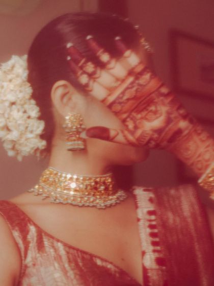 A shy, playful moment as the bride covers her face with her henna-adorned hand. The warm, reddish tones and soft focus make this an intimate and artful bridal portrait.