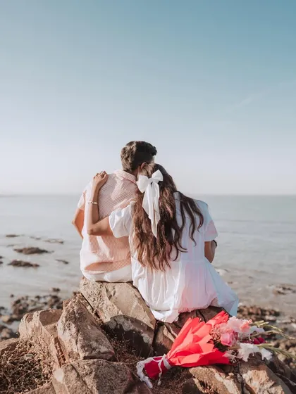 A quiet moment together, watching the sun set over the ocean. This pre-wedding shot captures the romance and anticipation before the big day, with a beautiful bouquet adding a pop of color to the serene seascape.