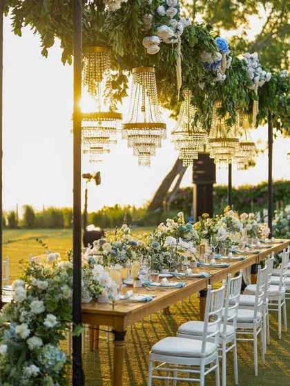 Long table guest seating at a beautiful sunset garden wedding, with hanging chandeliers and floral arrangements creating a magical ambiance.