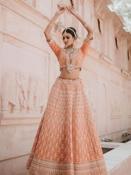 A peach-colored lehenga with intricate white embroidery, shot against a heritage backdrop. The full-length and twirling shots show its grace and elegance.