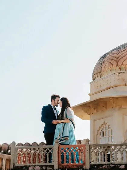 A romantic portrait on the ramparts of a fort, with a historic dome in the background, capturing the essence of a royal love story.