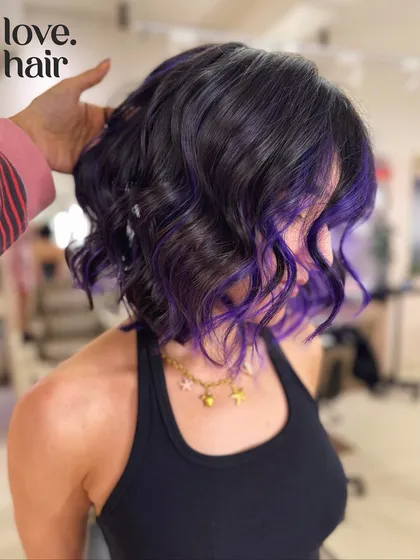 A hint of purple aura. We added these cool purple peekaboo highlights to a short, wavy bob for a fun pop of color. This look was created using a bleach and tone vivid color technique.
