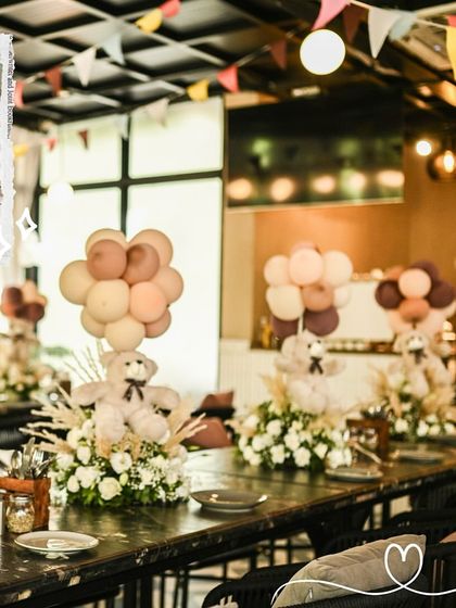 Table centerpieces for the boho teddy bear shower. Each table features a plush bear with a balloon bouquet, surrounded by white flowers and dried pampas grass for a rustic yet elegant look.