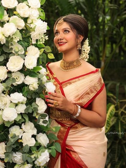 Portraits from a makeup shoot, showcasing a model in a classic red and cream saree. The images highlight the flawless makeup and traditional styling in a beautiful garden setting.