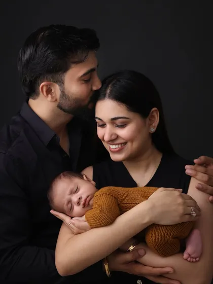A modern family portrait with a classic feel. The dark, moody background creates a dramatic and intimate feel, making the connection between the parents and their newborn the central focus of this beautiful image.