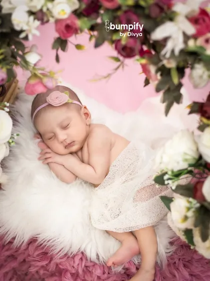 A close-up of the newborn sleeping on a soft white rug, framed by a beautiful floral wreath. This angle highlights the baby's delicate features and peaceful expression.