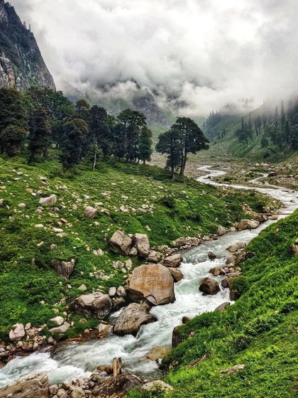 A stream flowing through the rocky, green landscape of the Hampta Pass valley.