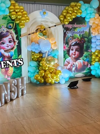 A different angle of the Little Krishna naming ceremony, showing the details of the balloon arches in gold, teal, and orange, framing the central backdrop.