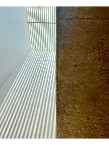The dynamic play of sunlight through a skylight creates moving patterns on a wall, contrasting with the static, rough texture of a board-formed concrete surface. This is from our "Colour Splash House" project.