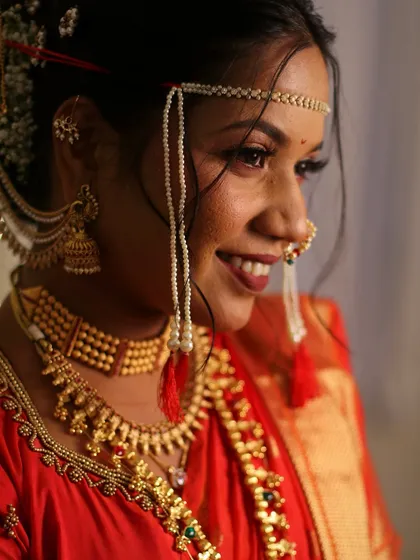 A close-up of a bride in a stunning red Nauvari saree. The look features a classic winged eyeliner, a traditional nath, and a beautiful Khopa hairstyle adorned with flowers.