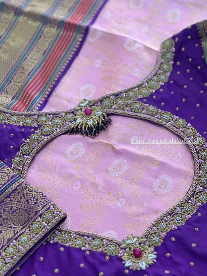 A deep back cutout on a purple blouse, featuring an intricately embroidered border and a tassel detail. The design is set against a light pink brocade fabric.